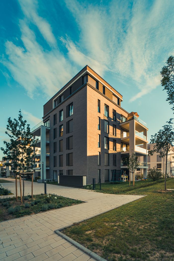 about-img Contemporary apartment building exterior with landscaped surroundings under a clear sky.