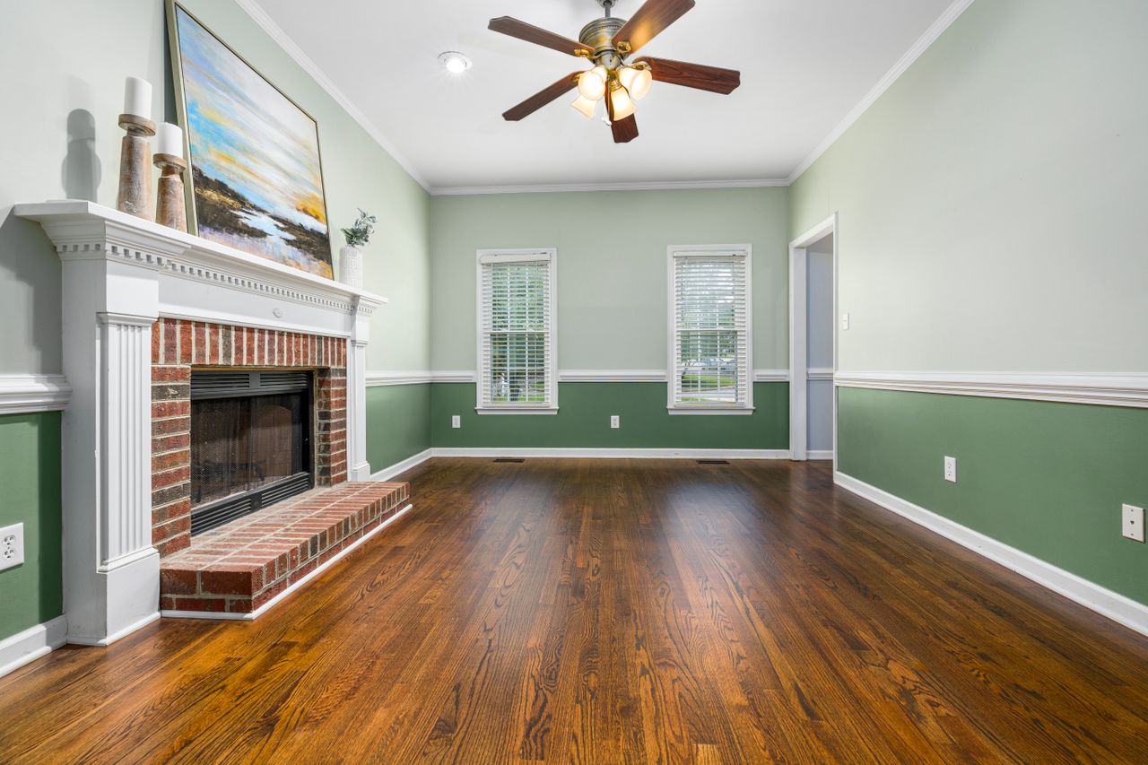 services-02 A cozy empty living room featuring a brick fireplace, wooden floors, and elegant decor.